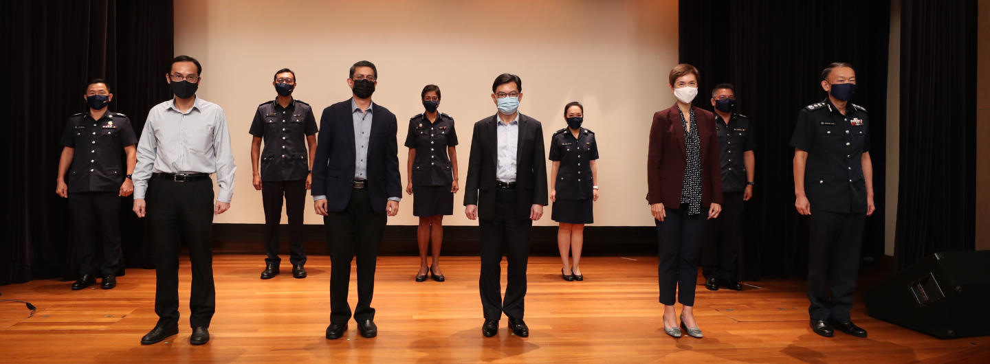Group of uniformed and civilian people with face masks on wooden stage.